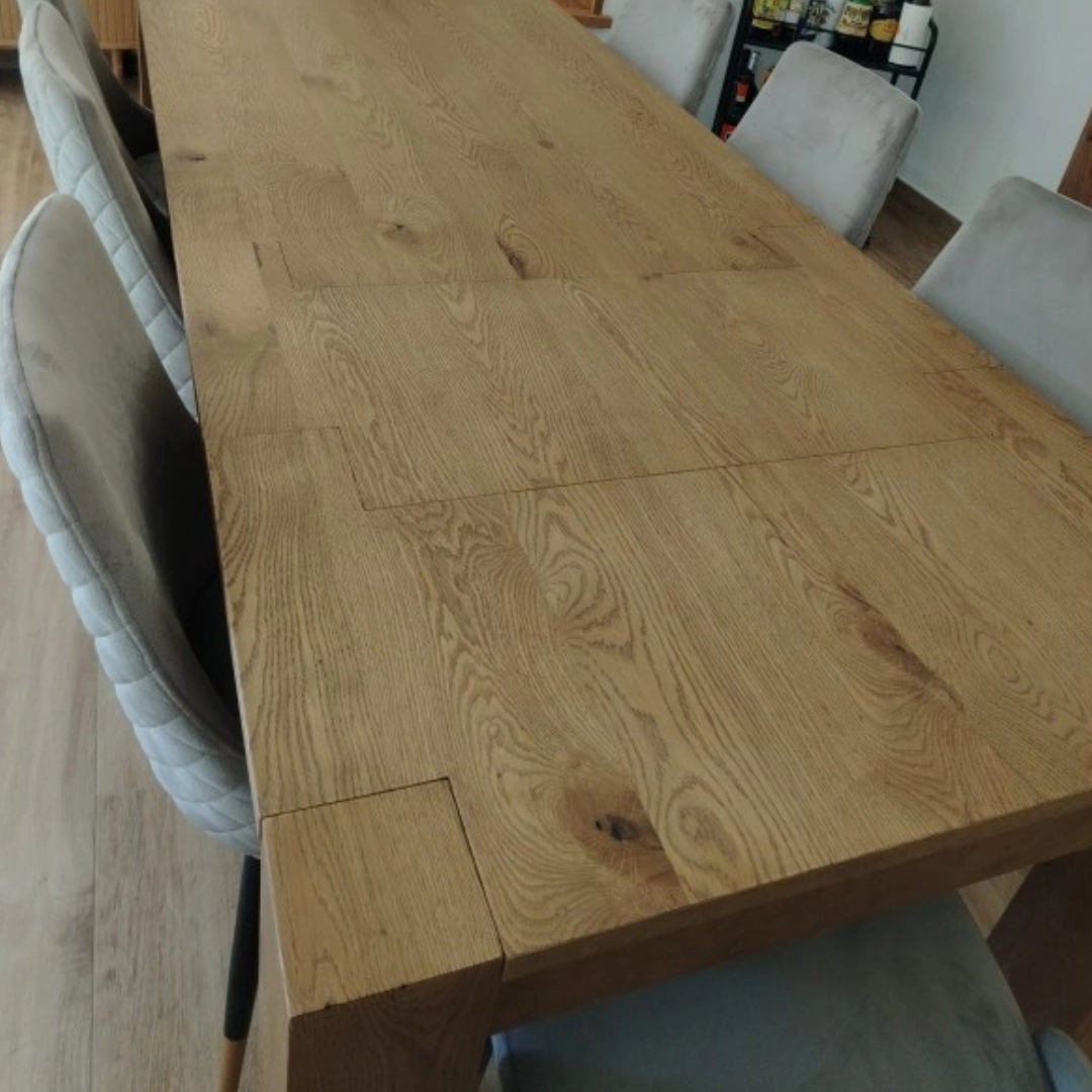 Superficie del tavolo allungabile Marca Design Shop in rovere con venature ben visibili, con dettaglio delle sedie imbottite grigie sullo sfondo.