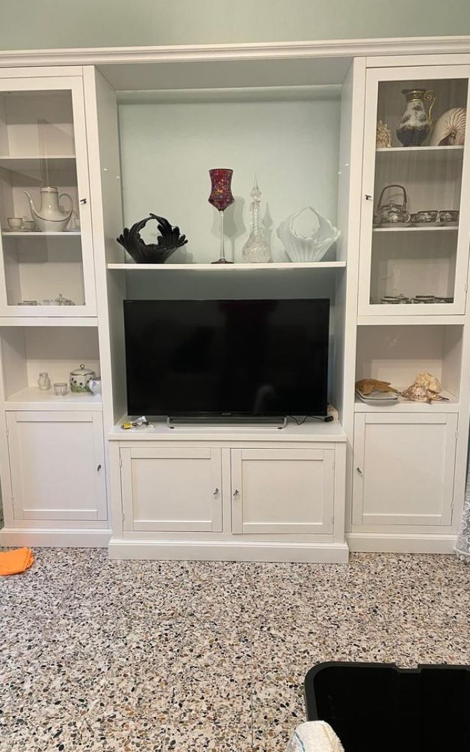 Parete attrezzata bianca opaca con vano porta TV centrale, vetrine laterali e oggetti decorativi.