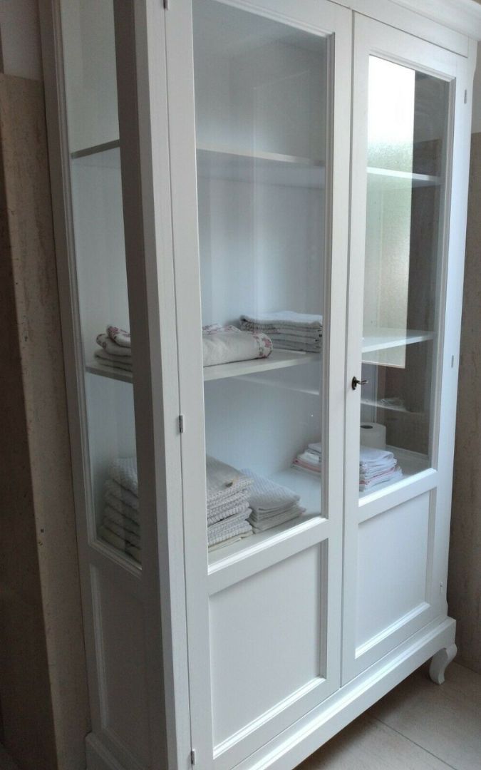 Interno di vetrina in legno bianco con piatti, bicchieri e stoviglie in esposizione.