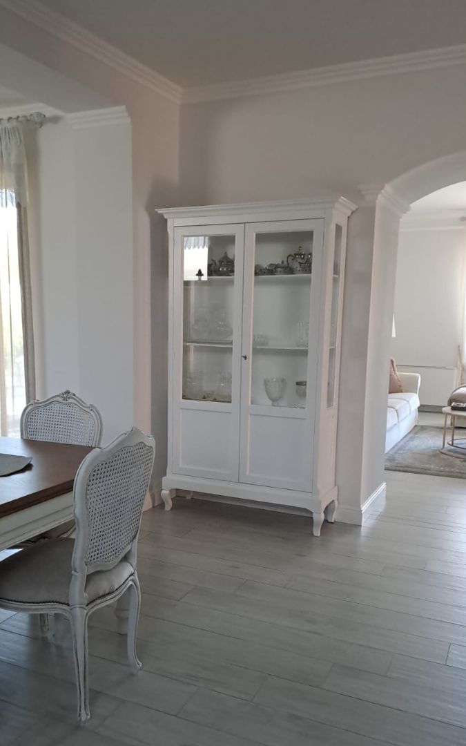 Vetrina in legno bianco stile Arte Povera posizionata in una sala da pranzo luminosa.